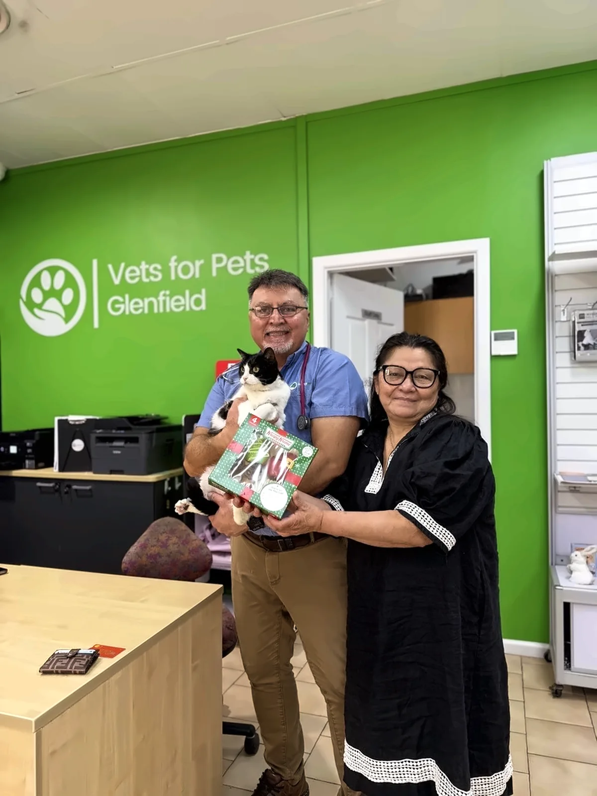 A Vets for Pets veterinarian holding a black-and-white cat with its owner at the Glenfield reception desk
